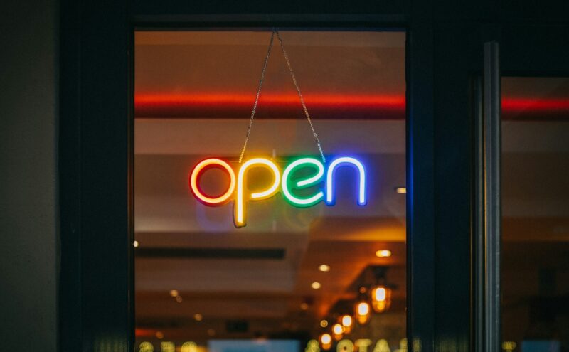 Ein buntes Neonschild mit der Aufschrift "open" hängt an einer Glastür.